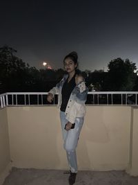 Portrait of young woman standing by railing against sky