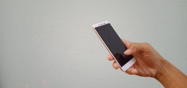 Midsection of person holding mobile phone against wall
