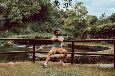 Portrait of young woman sitting on railing against trees