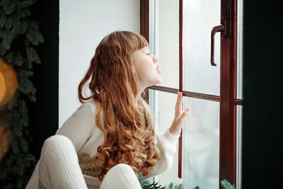Happy young girl sitting by the window and christmas tree