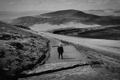 Rear view of boy walking on mountain against sky