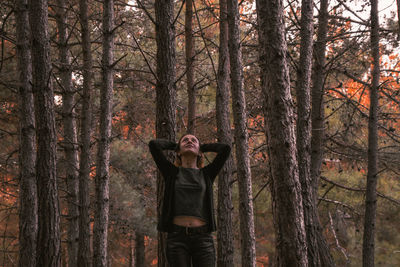 Woman standing by tree trunk in forest