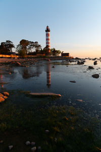 Lighthouse by sea against sky during sunset