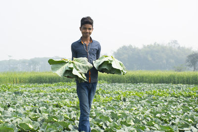 Portrait of a smiling young farmer standing on field carrying cabbage