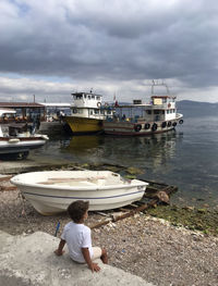 Rear view of man sitting on boat moored at shore against sky