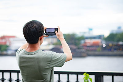 Rear view of man photographing while standing by railing