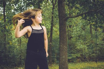 Girl tossing hair while standing against trees in forest