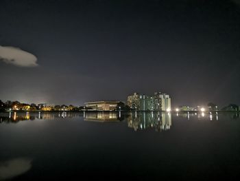 Illuminated buildings by sea against sky at night