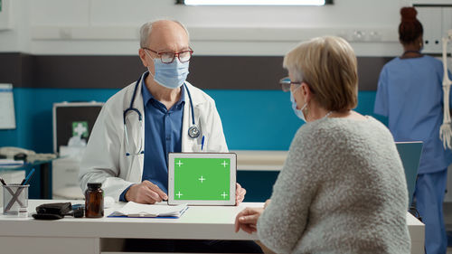 Senior doctor showing digital tablet screen to patient at clinic