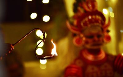 Cropped hand holding oil lamp with man wearing costume during celebration