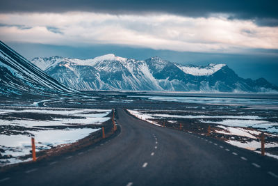 Road leading towards snowcapped mountains against sky