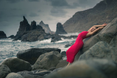 Young woman with arms raised leaning on rock at beach