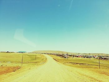 Road amidst field against clear blue sky