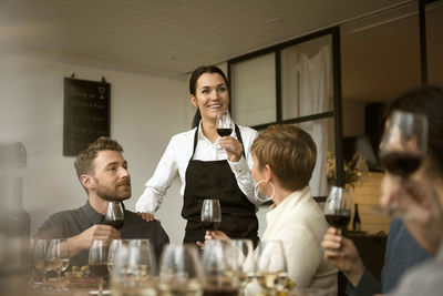 Smiling woman wearing apron holding wineglass with business people at table