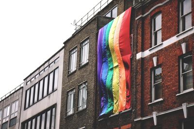 Low angle view of multi colored flag hanging on building against sky