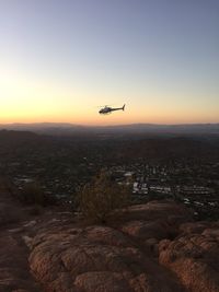 Airplane flying over cityscape against sky during sunset