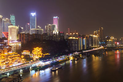 Illuminated buildings by river against sky in city at night