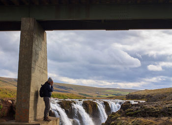 Man standing under bridge against waterfall