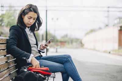 Woman using mobile phone while sitting on bench