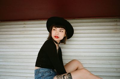 Young woman looking away while sitting by wall