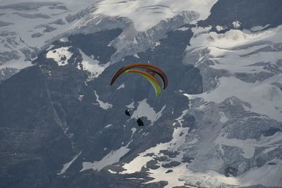 Person paragliding over snowcapped mountain