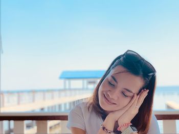 Smiling young woman with eyes closed and head cocked against sky