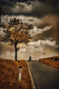 Road passing through field against cloudy sky