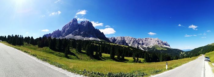 Panoramic view of road by mountains against blue sky