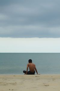 Rear view of shirtless man looking at sea against sky