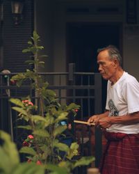 Senior man standing by plant against fence in yard