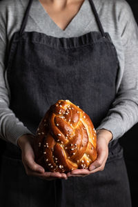 Crop housewife in apron holding appetizing tasty homemade braid bread with sprinkles