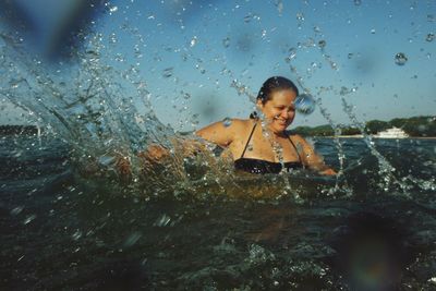 Smiling overweight woman splashing water in sea