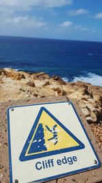 Close-up of information sign on beach against sky