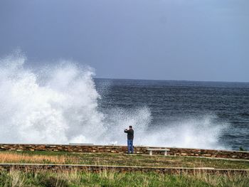 Rear view of man photographing wave splashing on shore