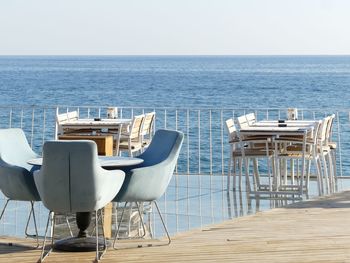 Chairs and table by sea against clear sky