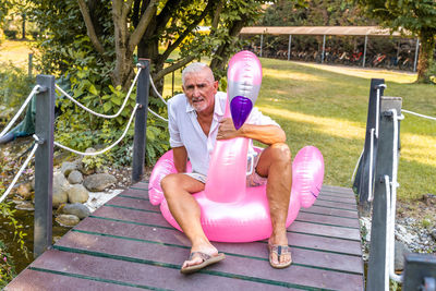 Portrait of smiling handsome middle aged man sitting on an inflatable pink flamingo toy