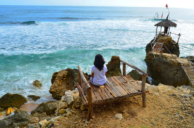 Rear view of man sitting on rock by sea