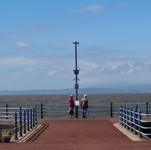 Rear view of people walking on sea shore against sky