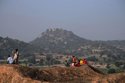 People sitting on rock against mountain range against clear sky