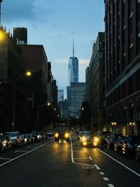 Cars on city street amidst buildings against sky at dusk