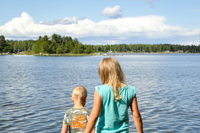 Rear view of friends against lake against sky