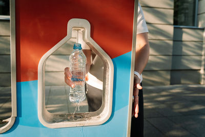 Woman pours clean drinking water into bottle at drinking water refill station in city street