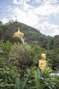 Statue against trees and plants against sky