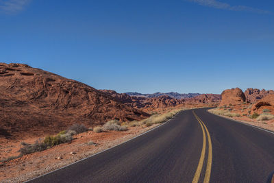 Empty road amidst desert against clear blue sky