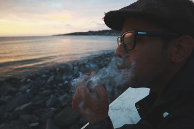 Side view of man smoking cigarette at beach during sunset