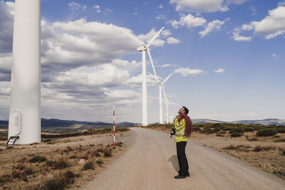 Technician with rope standing on road looking at wind turbine