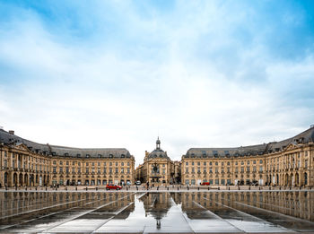 Place de la bourse and wet walkway against cloudy sky in city