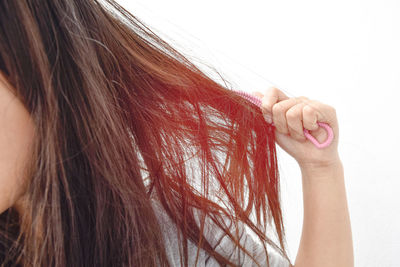 Cropped image of woman combing tangled hair against white background