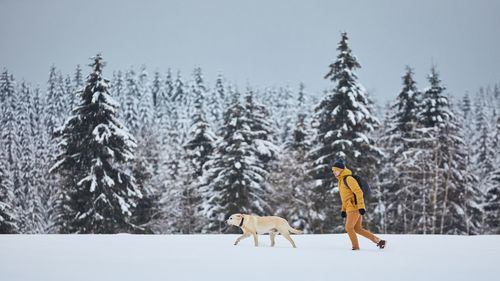 Side view of man with dog walking on snow covered landscape