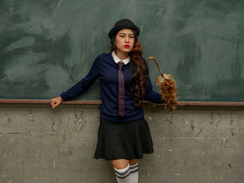 Portrait of young woman standing against wall